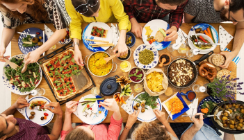 Mit vielfältigen, bunten Speisen gedeckter Tisch, an dem mehrere Personen sitzen