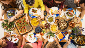 Mit vielfältigen, bunten Speisen gedeckter Tisch, an dem mehrere Personen sitzen