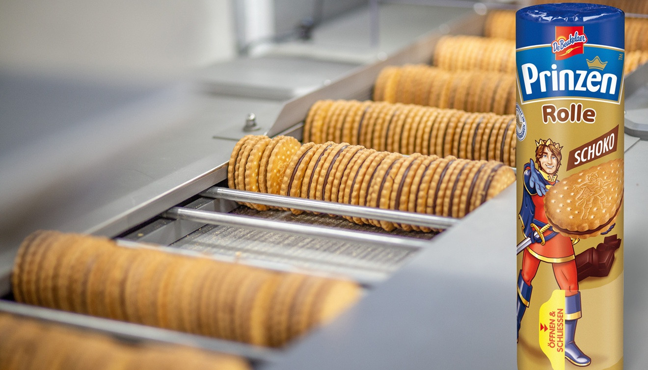 Verschlossene Prinzenrolle vor Produktionsband mit unverpackten Prinzenrolle-Keksen