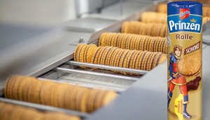 Verschlossene Prinzenrolle vor Produktionsband mit unverpackten Prinzenrolle-Keksen