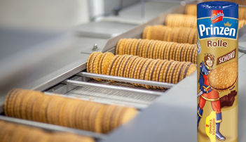 Verschlossene Prinzenrolle vor Produktionsband mit unverpackten Prinzenrolle-Keksen